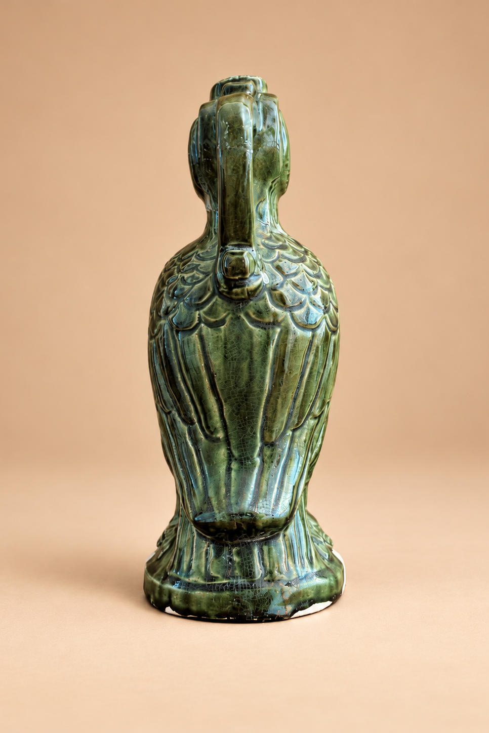 An antique green glazed ceramic bird figurine, likely a phoenix or dragon, standing upright against a solid beige background.
