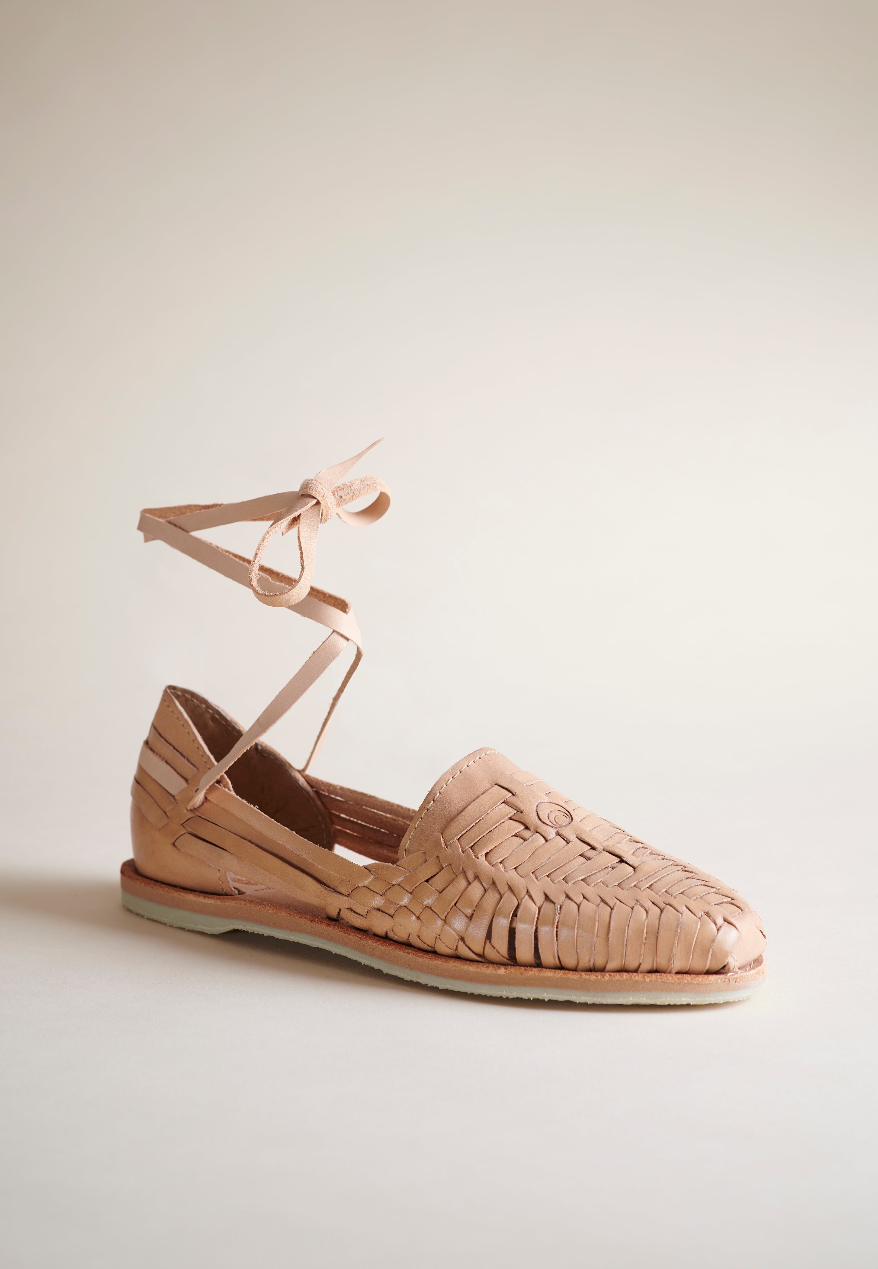 A single tan woven leather flat with an ankle tie, shown from a side profile against a neutral cream background.