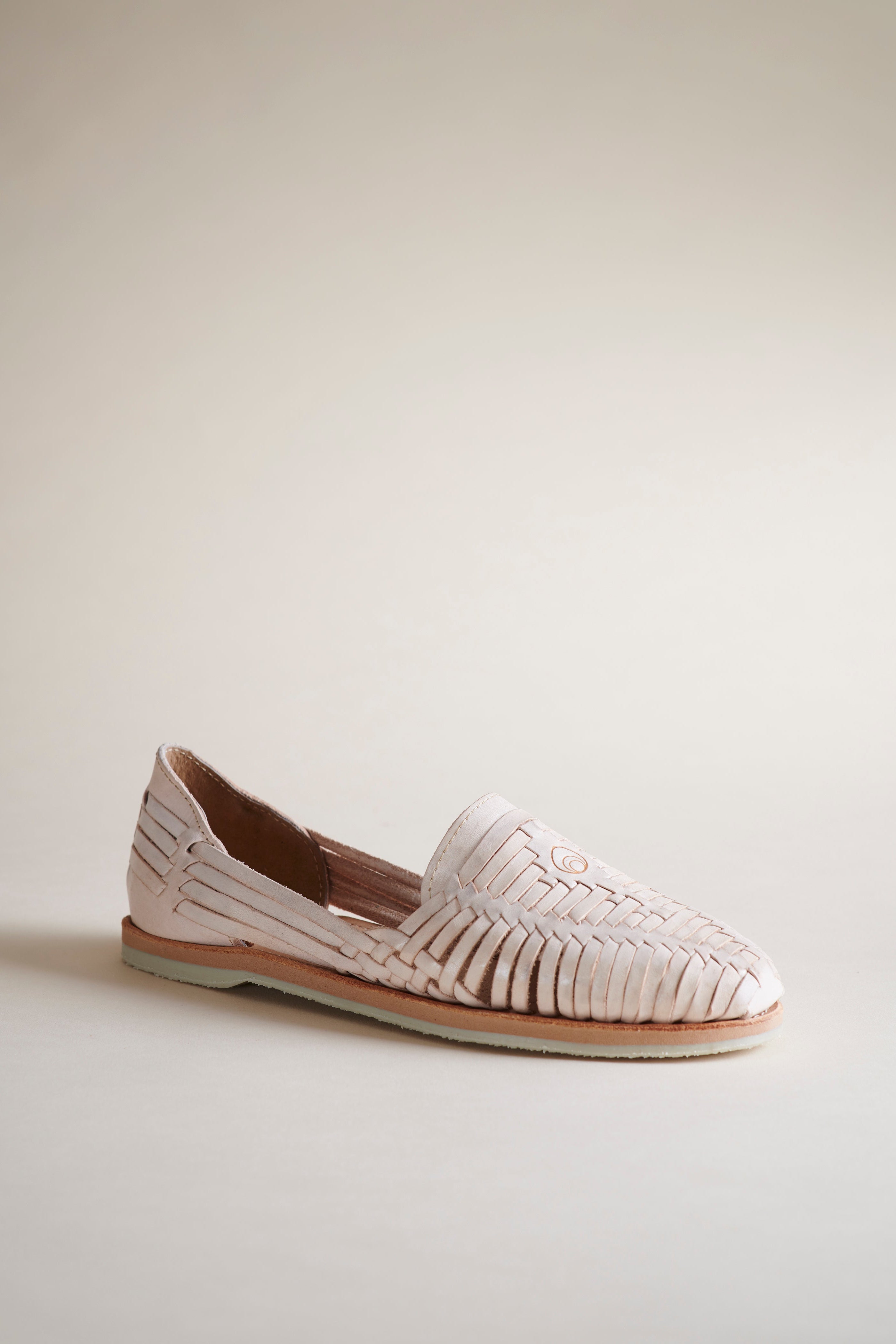 A single light pink woven leather loafer flat shoe with a tan sole, photographed on a clean, solid, warm off-white background.