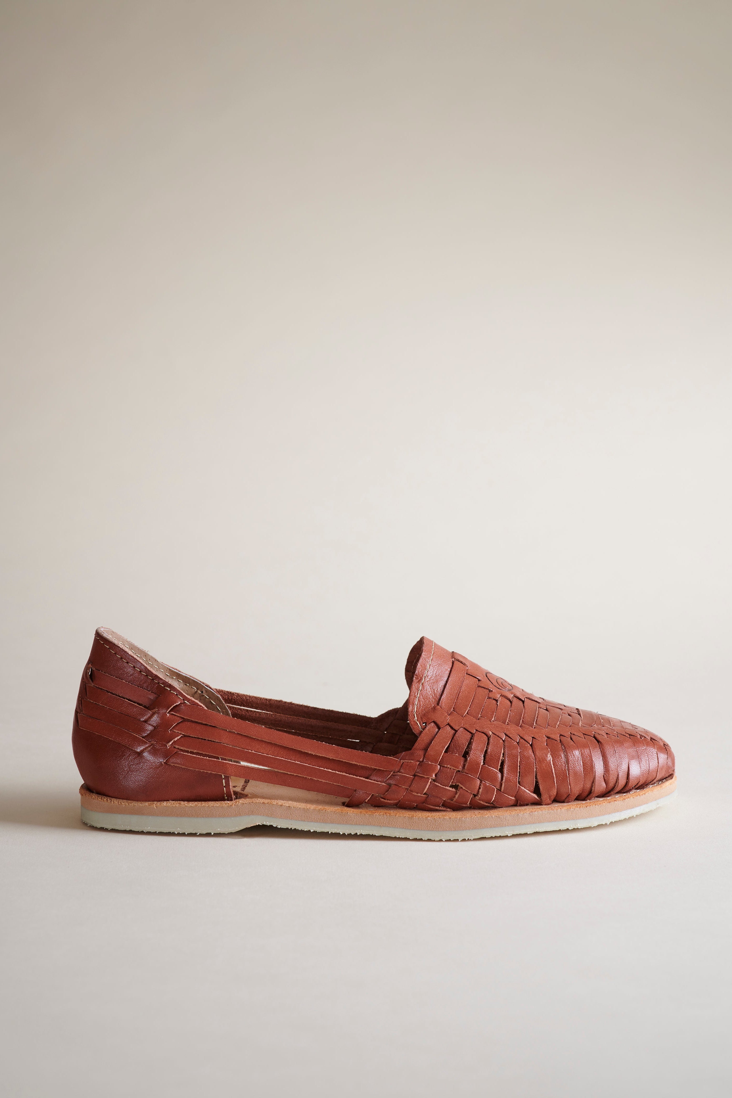 A single brown woven leather loafer shoe shown in profile against a plain, warm off-white background.