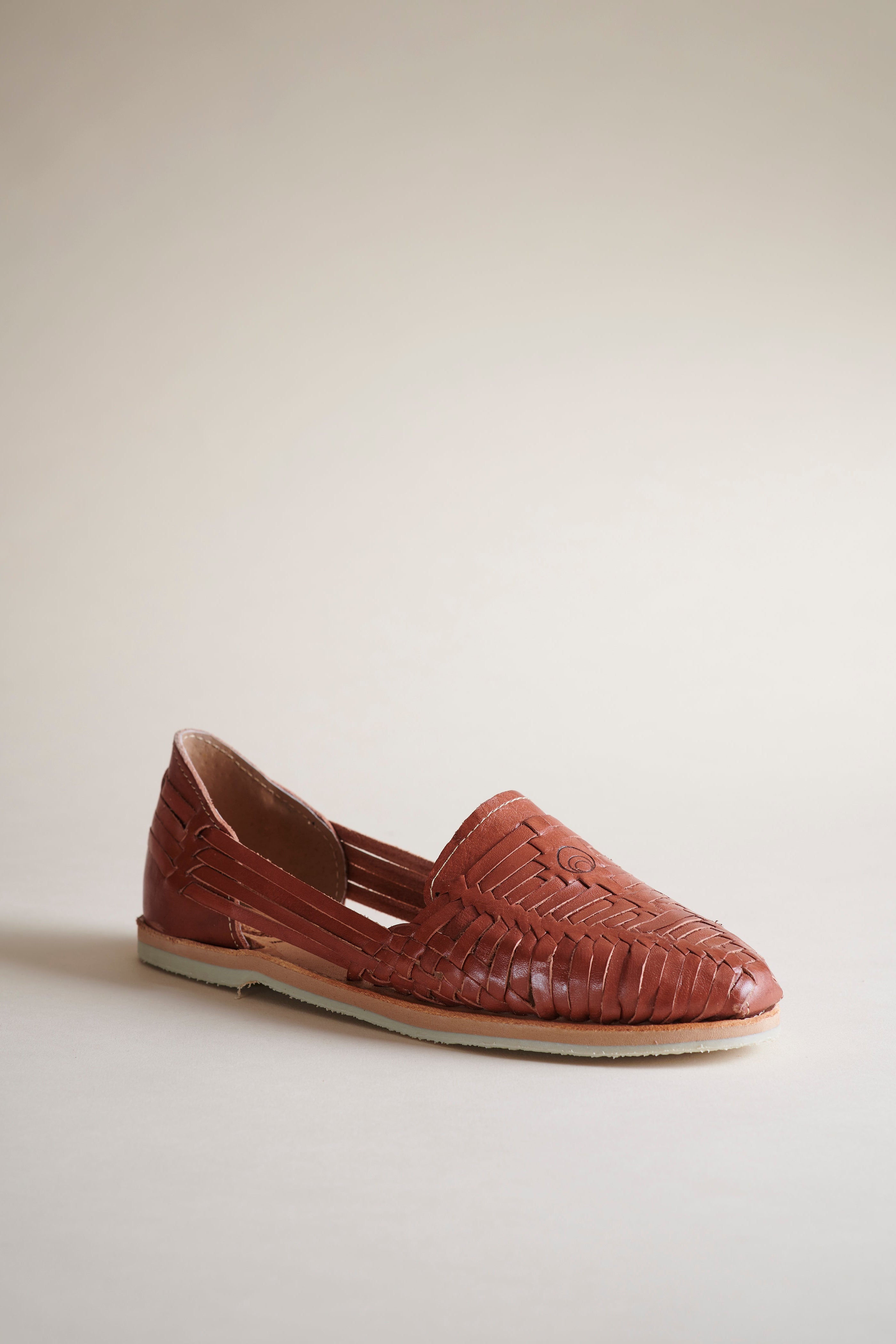 A single brown woven leather loafer slip-on shoe with a pointed toe, shown from a side profile against a neutral beige background.